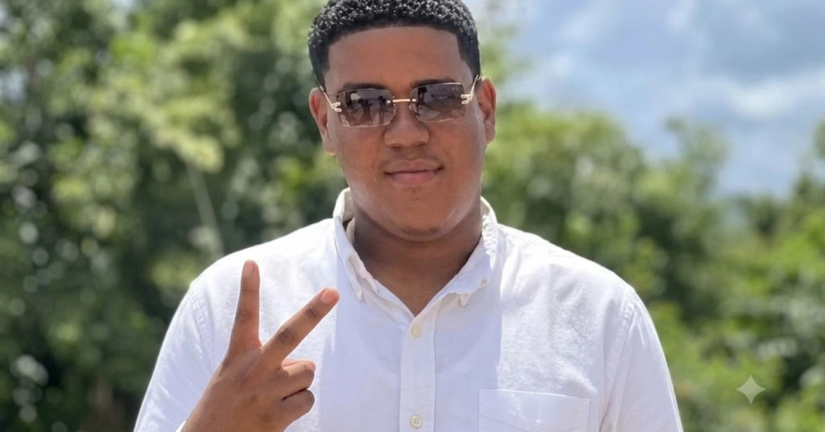 Young man in a white button-down shirt wearing sunglasses, outdoors, flashing a peace sign with green trees in the background.