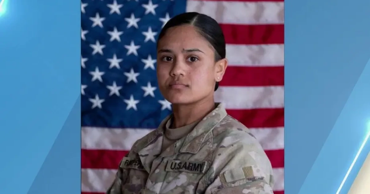 Female U.S. Army soldier in camouflage uniform stands in front of an American flag.