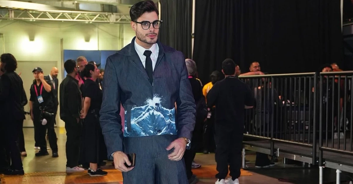 Man in a tailored blue-gray suit with a mountain-print panel at the waist, posing backstage among event staff and attendees.