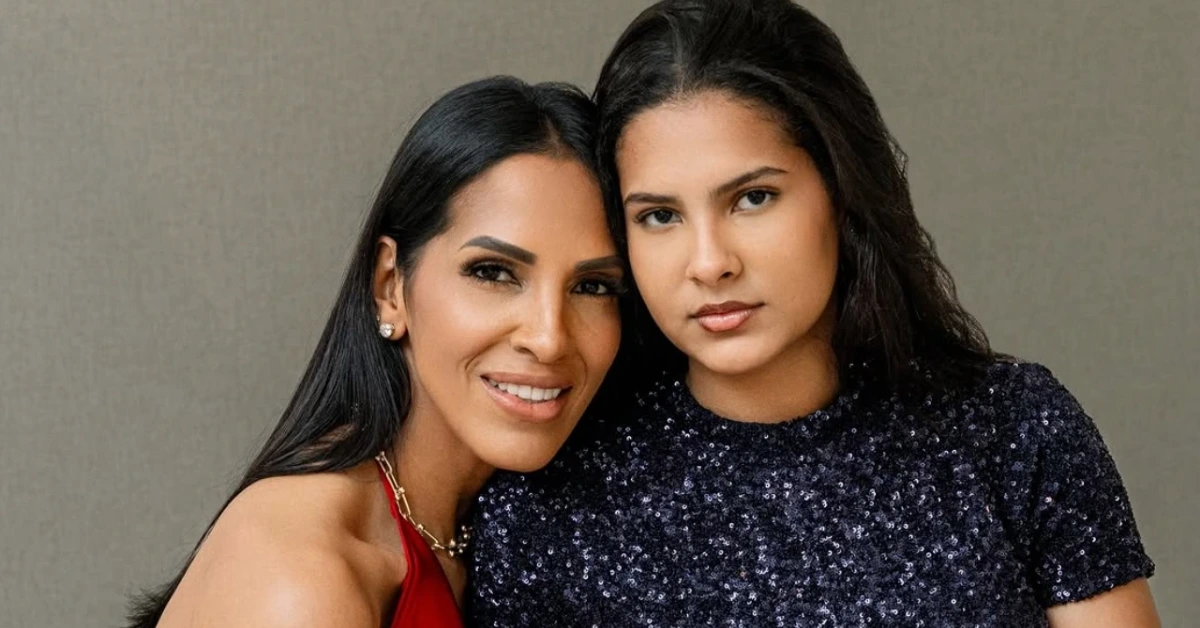 Two women posing closely for a photo, one in a red dress smiling beside a woman in a dark sequin top.