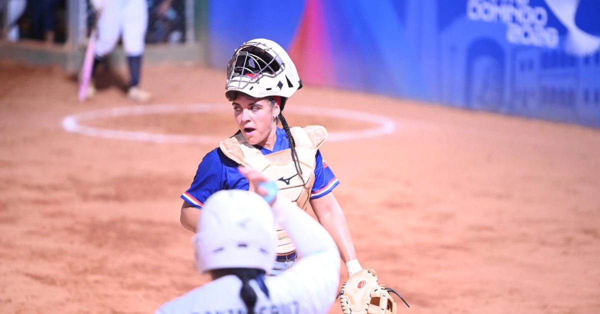 Female softball catcher in a blue uniform with helmet and chest protector, mid-throw on a dusty field.