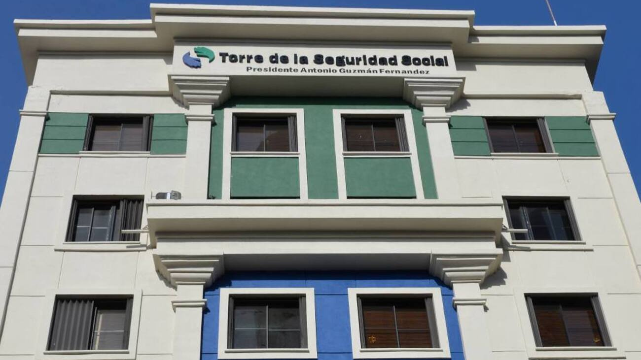 Facade of a light-colored building with green accents and a sign that reads 'Torre de la Seguridad Social' above a blue lower section.