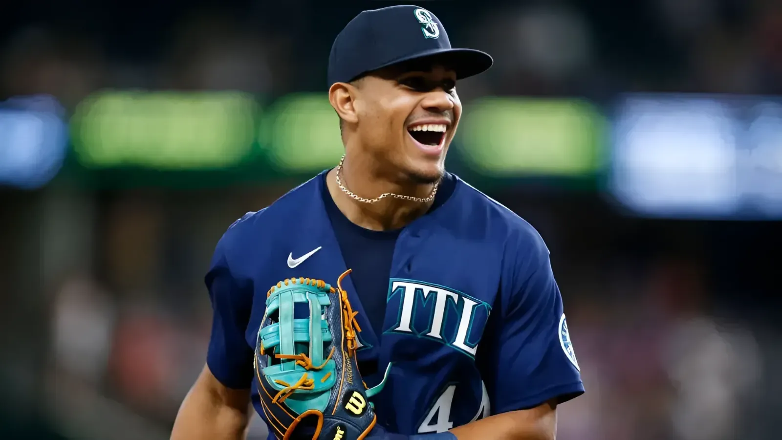 Baseball player in Mariners uniform laughing, holding a teal baseball glove.