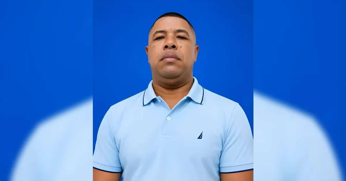 Portrait of a man in a light blue polo shirt standing against a solid blue background.