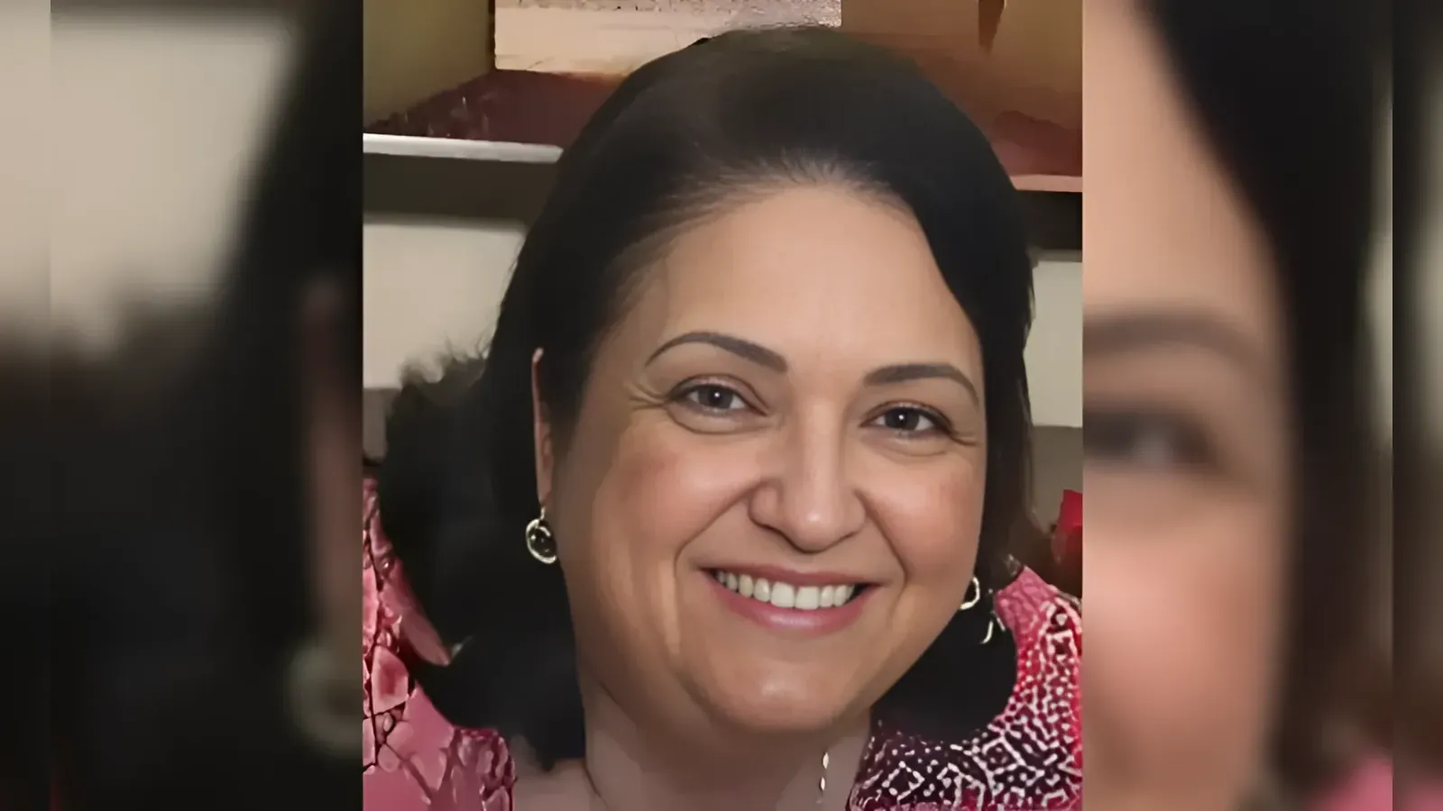 Smiling woman with short black hair, pink patterned top and hoop earrings (close-up portrait).