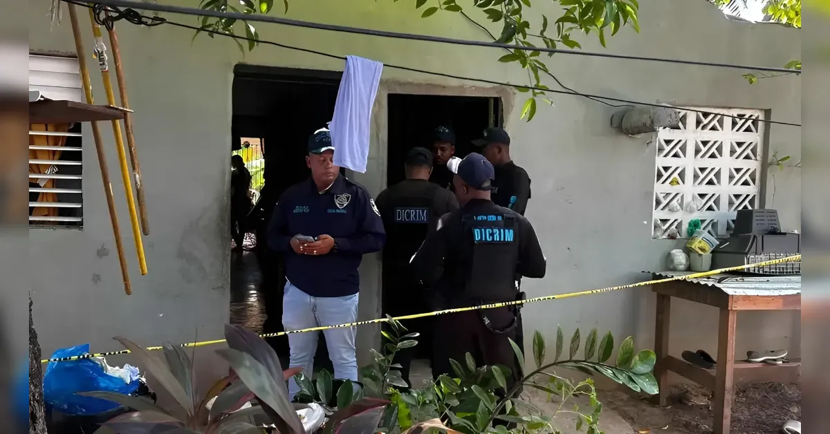 Group of investigators in dark uniforms stand at the doorway of a house, yellow tape cordons off the scene.