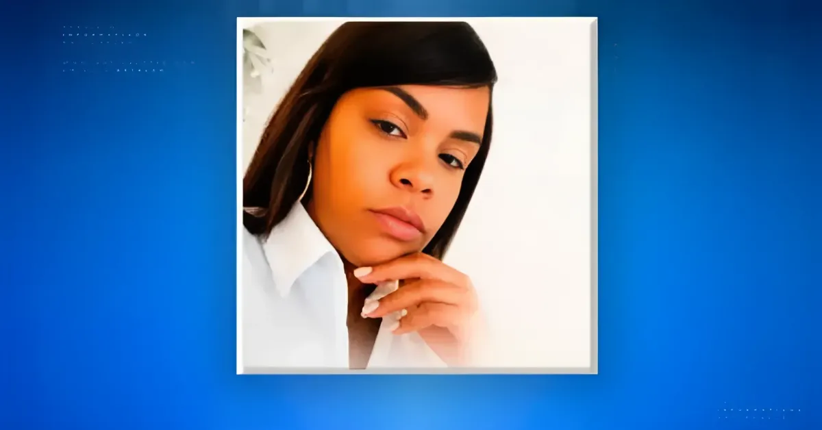 Portrait of a woman with dark hair in a white shirt, resting her chin on her hand, framed in a white square on a blue background wall.