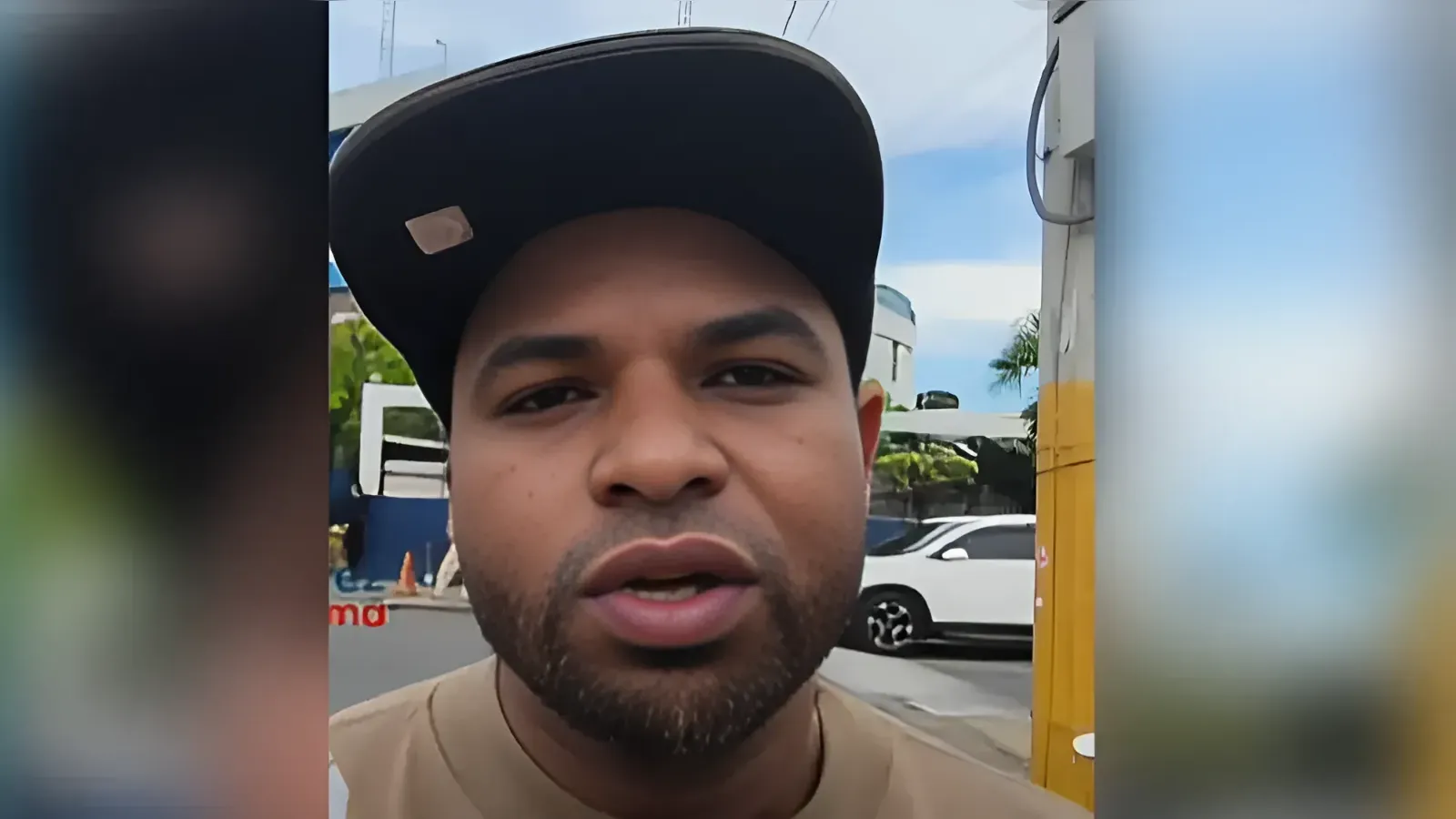 Close-up of a man wearing a black cap speaking to the camera outdoors.