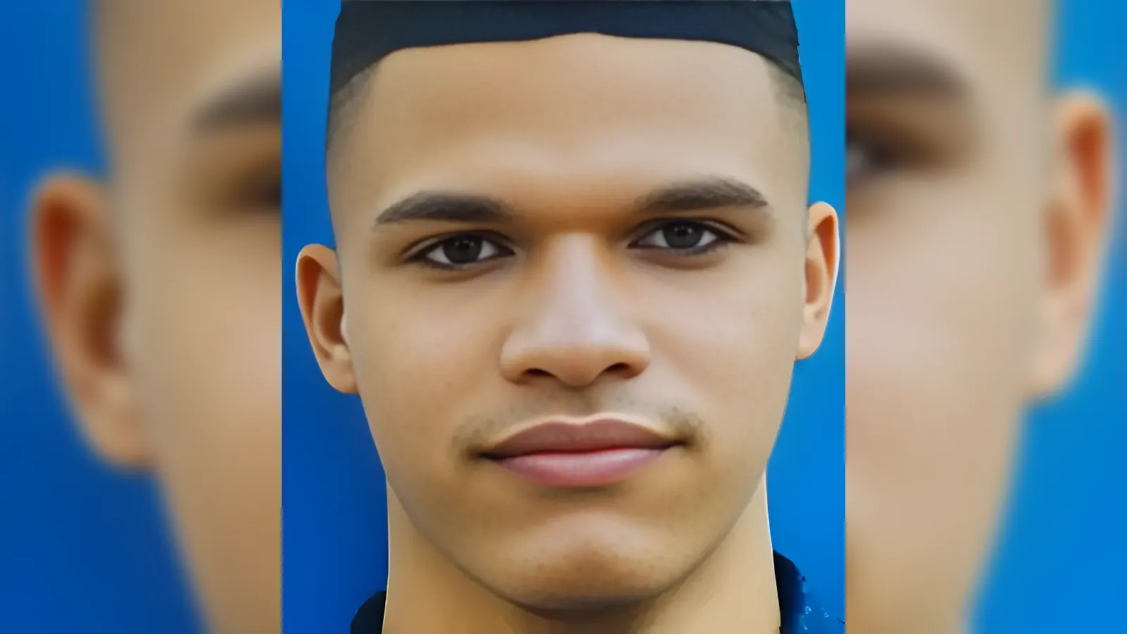 Close-up portrait of a young man wearing a graduation cap against a blue background, looking at the camera.