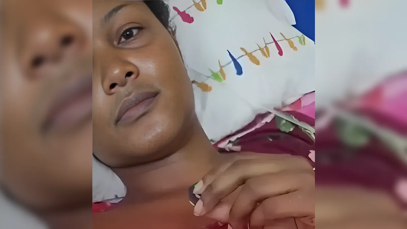 Close-up of a woman lying down, head on a pillow with colorful stitched patterns, hand resting on her chest.
