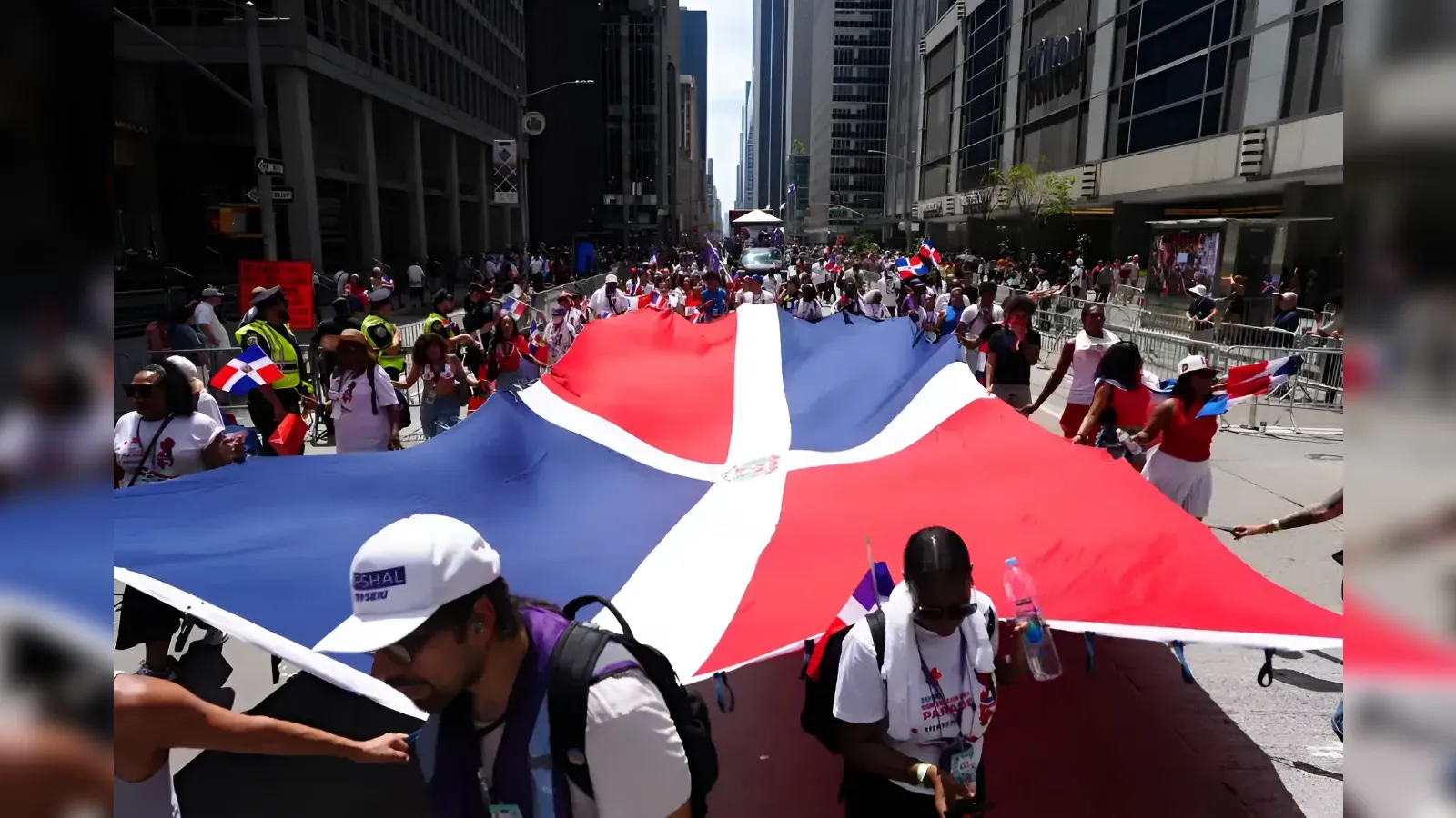 Crowd of marchers in a city parade carrying a giant Dominican flag banner across the street.