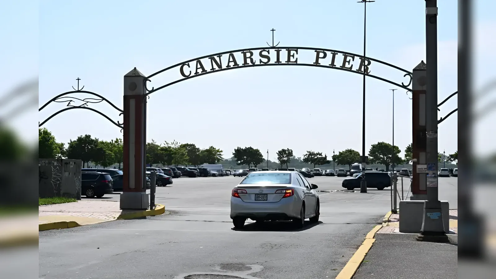 Arching gate reading 'Canarsie Pier' over a parking lot; white car driving through the entrance.