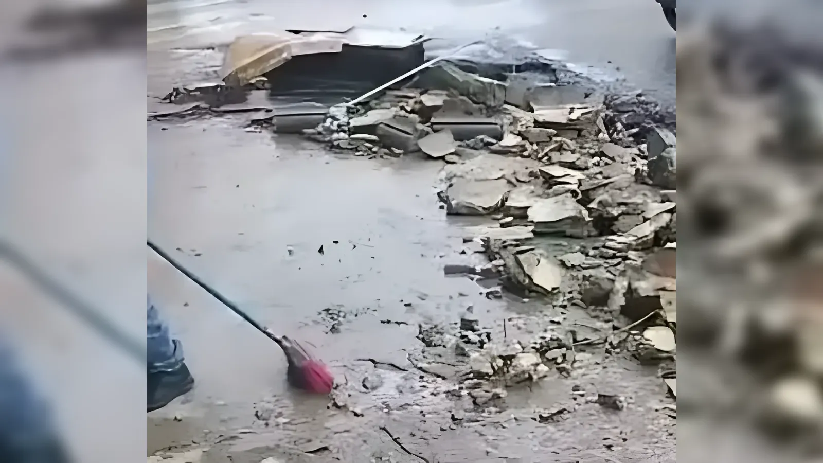 Person sweeping rubble and debris on a damaged street after a collapse, with broken concrete scattered around.