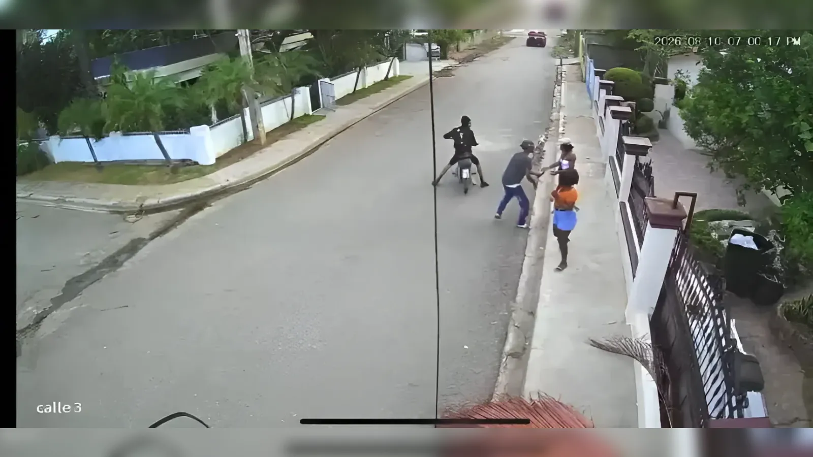 Surveillance footage of a residential street: a motorcyclist sits on a scooter while a small group of people argue on the sidewalk near a gate and wall.