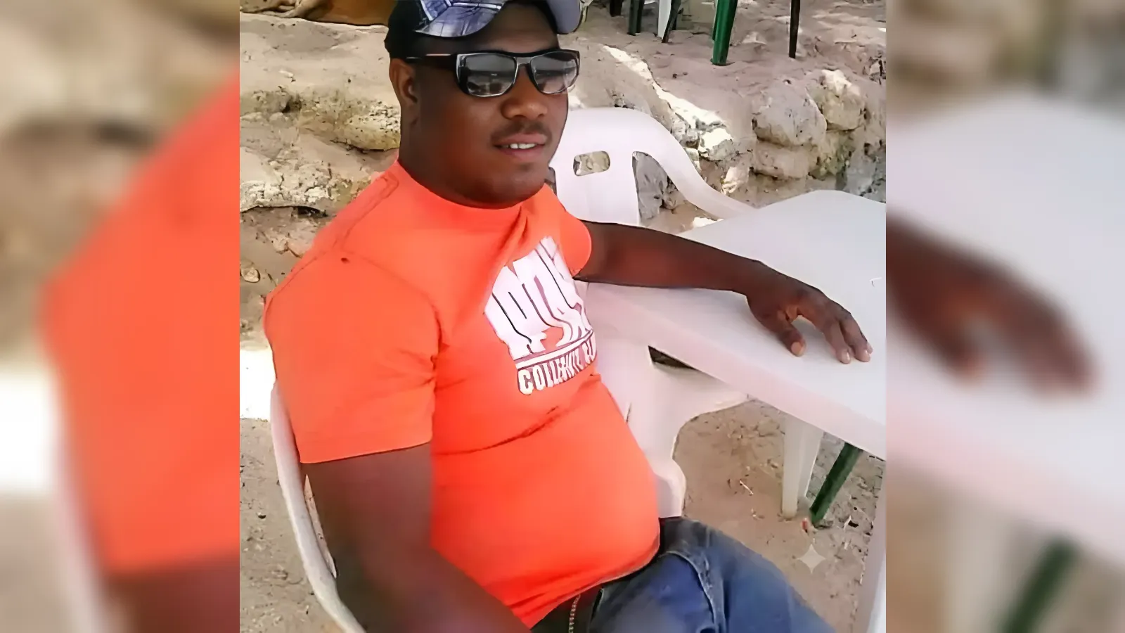 Man in an orange shirt and cap sits on a white plastic chair at a rocky beach, wearing sunglasses.