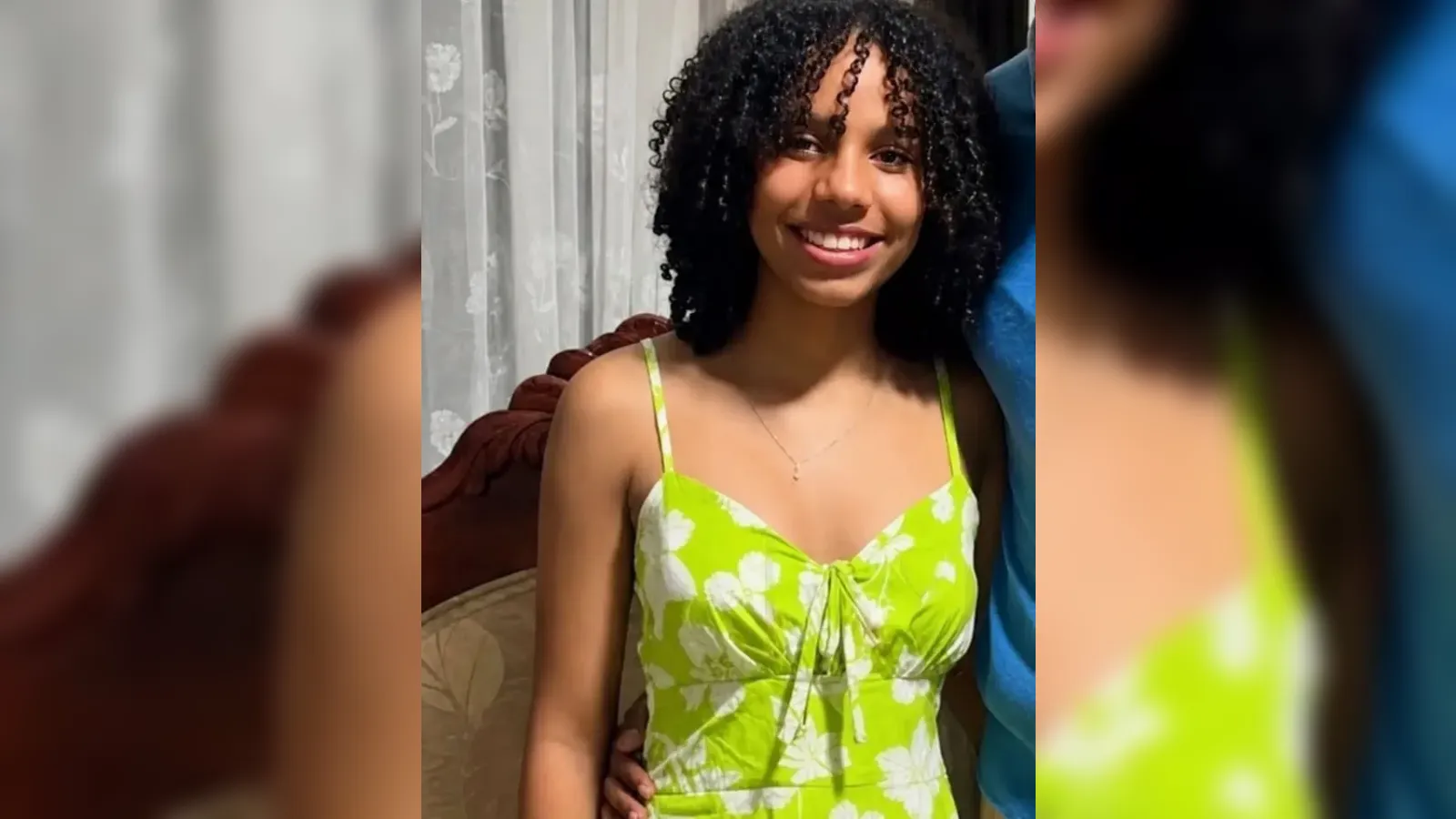 Smiling young woman with curly hair in a lime-green floral sundress indoors.