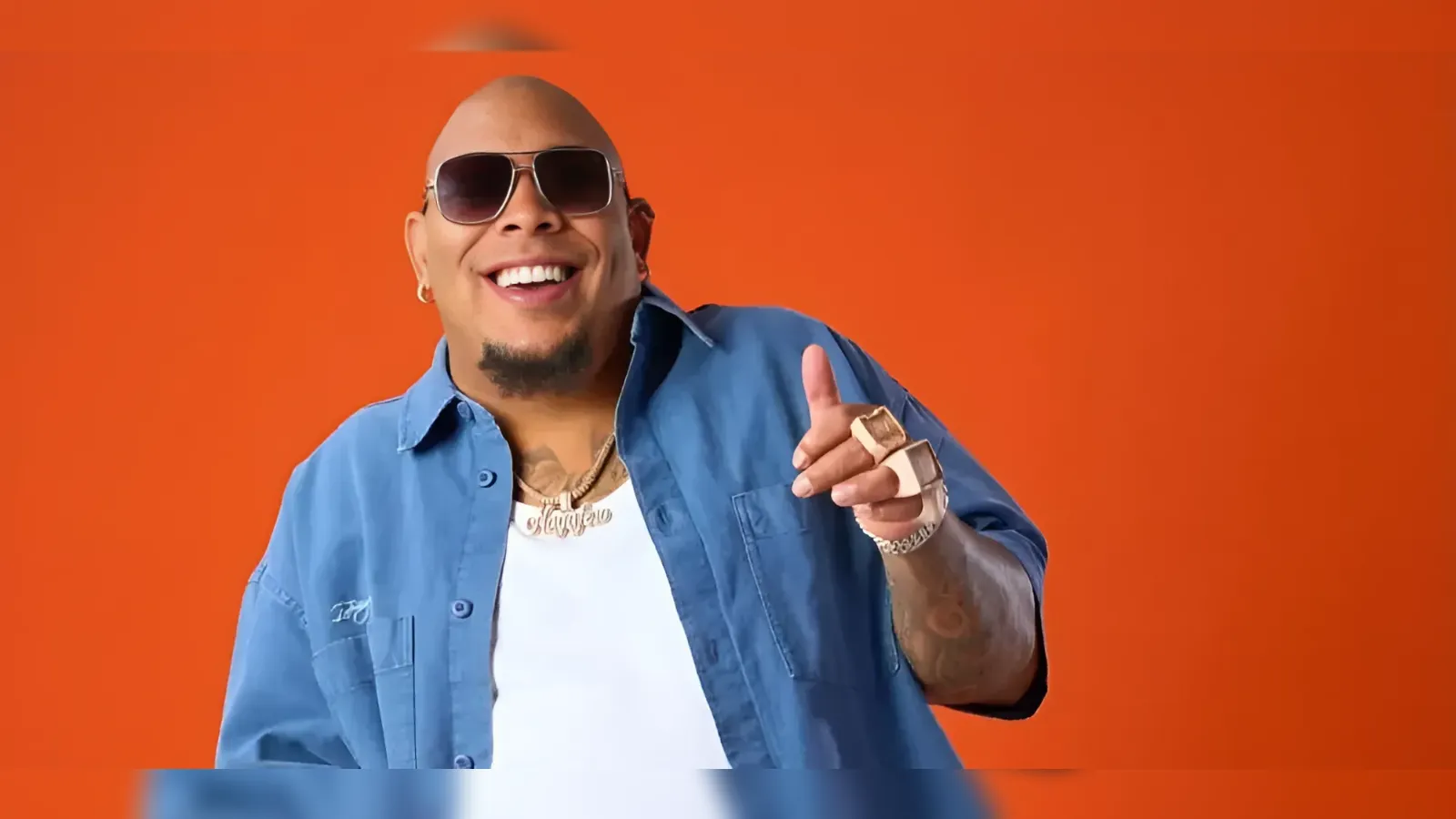Smiling man with sunglasses and a blue shirt points at the camera against an orange background.