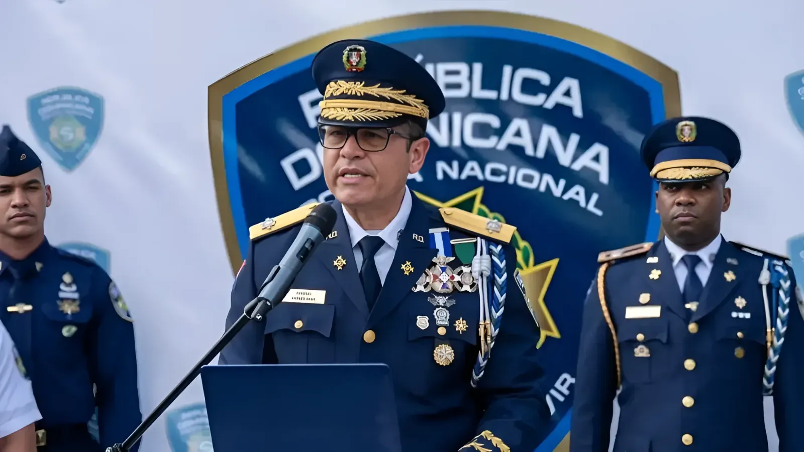 Senior police officer in dress uniform speaks at a podium during a formal ceremony, medals adorning his chest.
