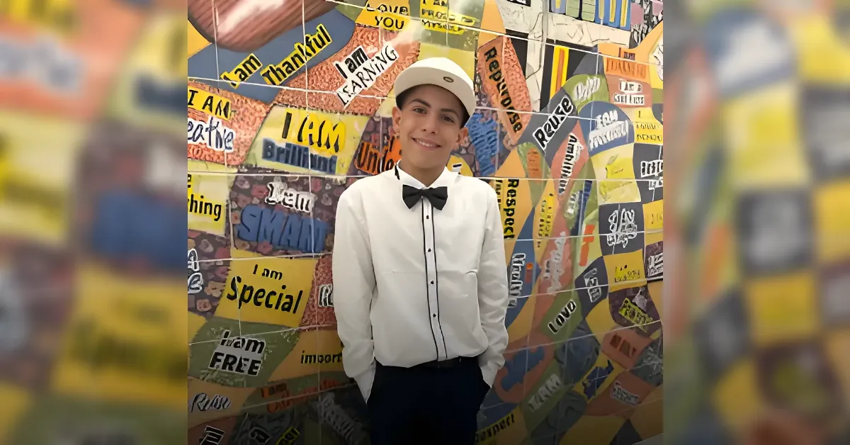 Smiling boy in a white shirt and bow tie stands in front of a wall covered with colorful taped quotes and phrases.