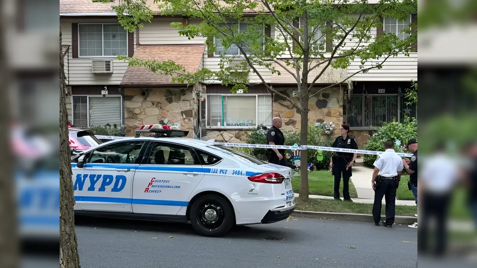 NYPD patrol car on a city street with crime-scene tape and police officers nearby, in front of a stone-faced apartment building.