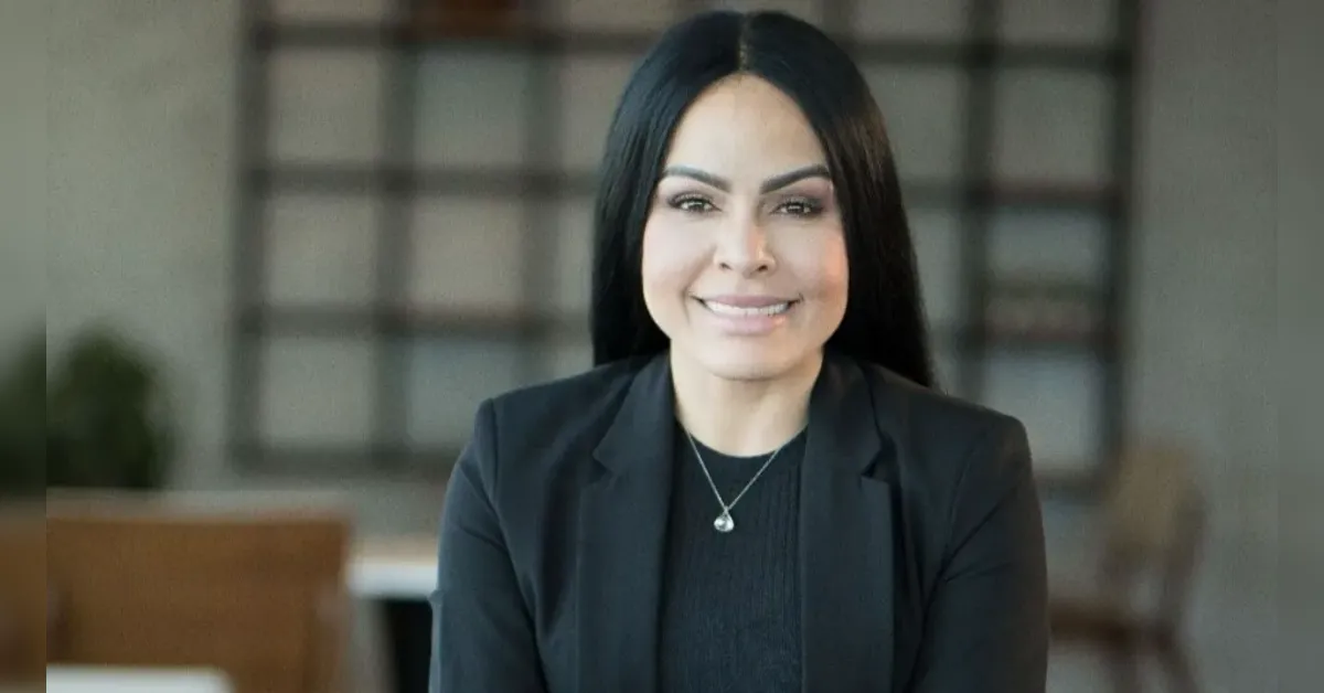 Professional woman with black hair in a dark blazer, smiling in an office setting.