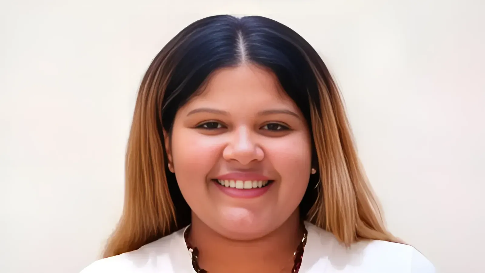 Portrait of a smiling woman facing the camera, with long dark-to-light brown hair and a white top.
