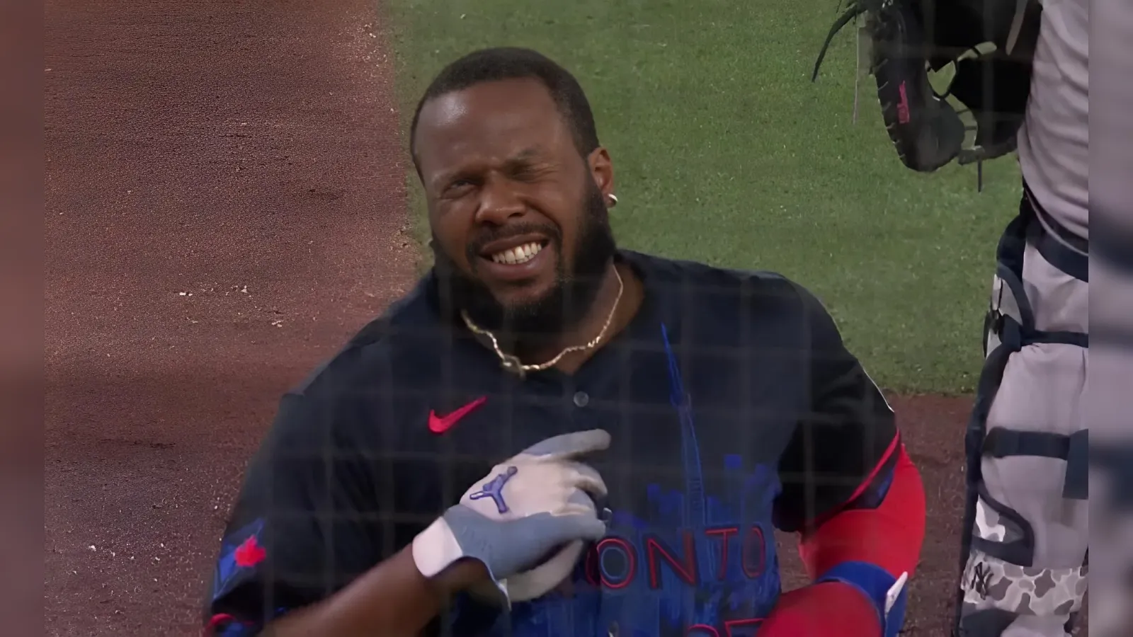 Baseball player in a dark Toronto jersey grimaces on the field as a teammate’s gloved hand touches his chest.