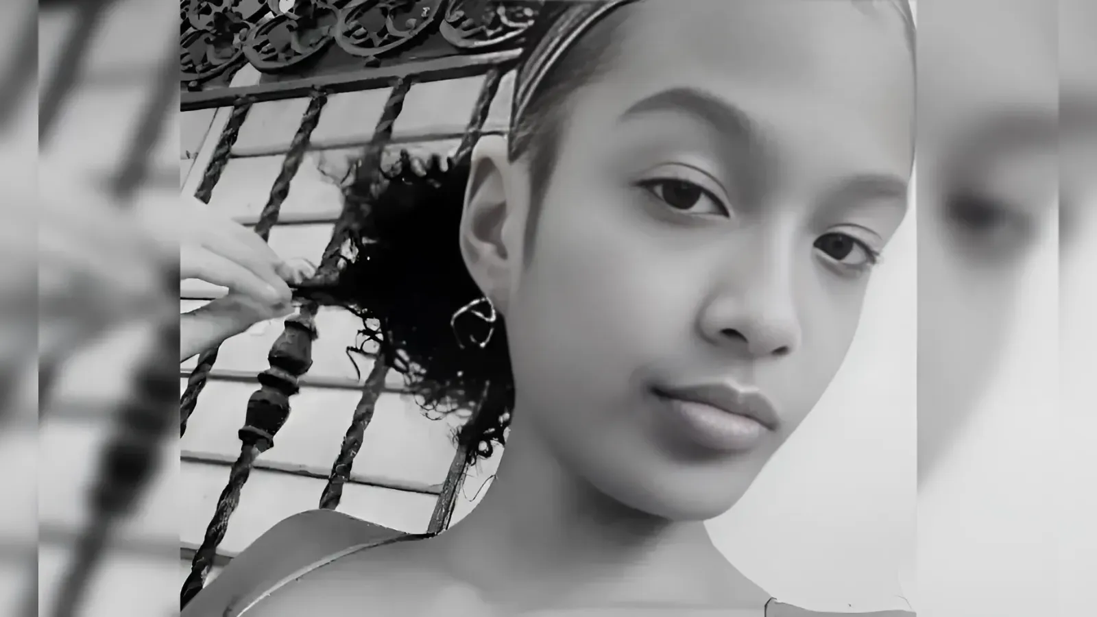 Black-and-white close-up portrait of a young woman looking at the camera, with an earring visible in one ear.