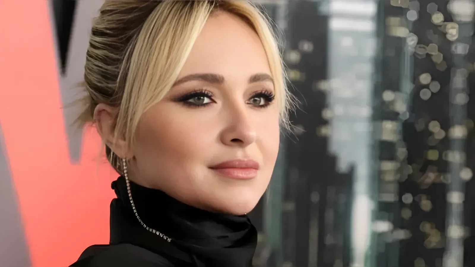 Close-up portrait of a blonde woman with makeup, wearing a black turtleneck and dangling earrings, looking slightly upward.