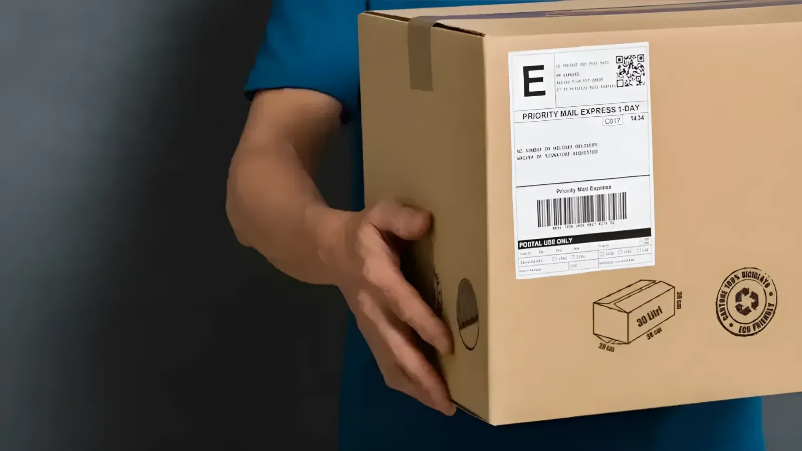 Close-up of a hand holding a brown cardboard box with a shipping label attached.