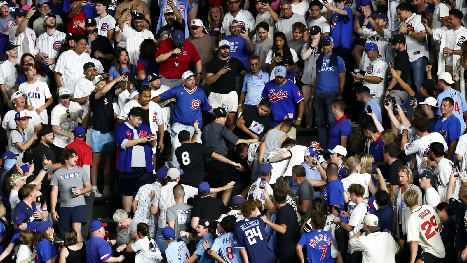 Large crowd of baseball fans packed into stadium stands, many wearing Cubs jerseys and hats, cheering and taking photos.