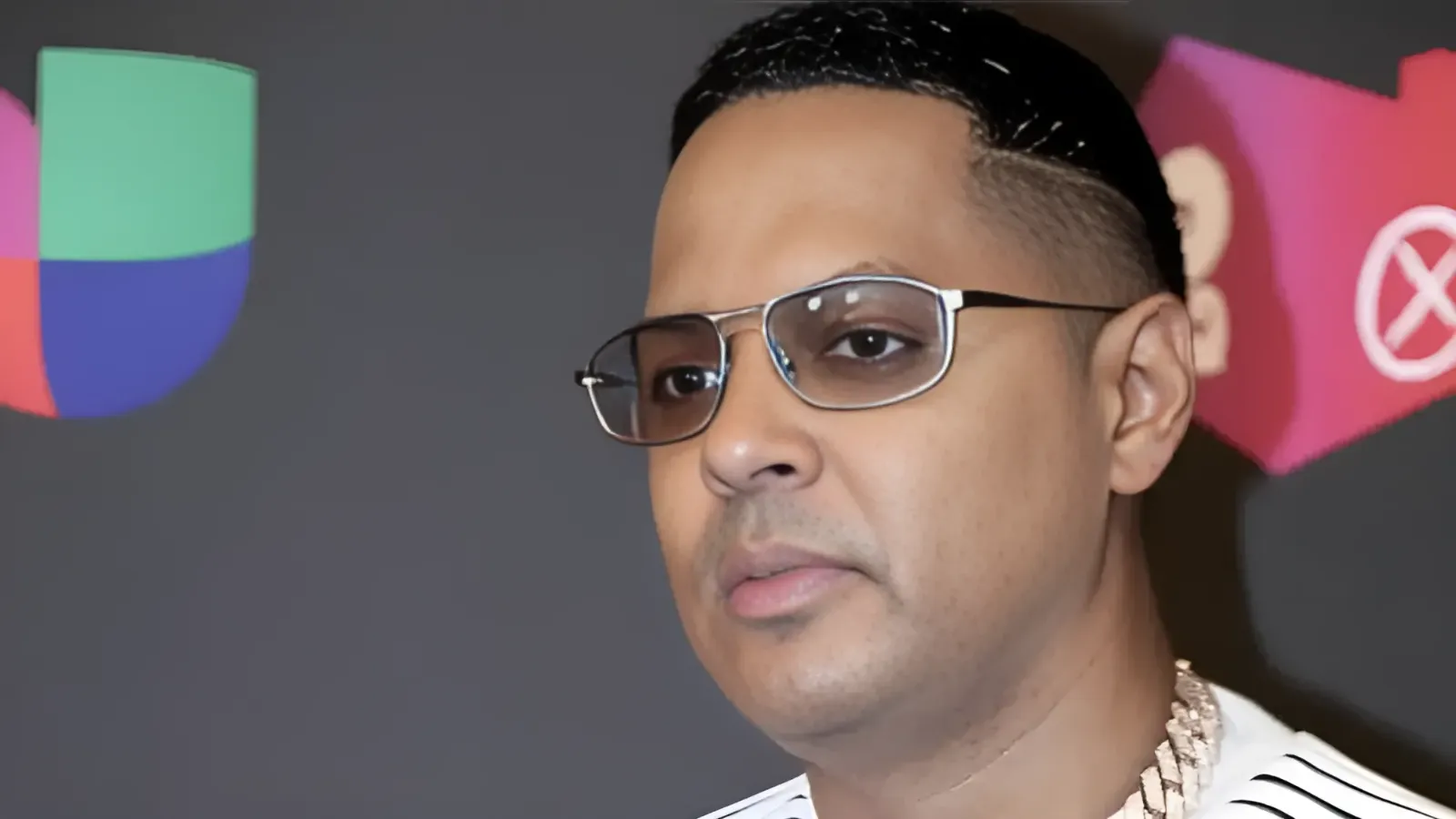 Close-up of a man wearing glasses at an event, with a colorful geometric backdrop behind him.