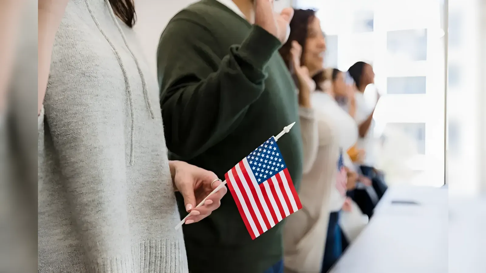 People standing in a line, each holding a small American flag in a bright, open space.