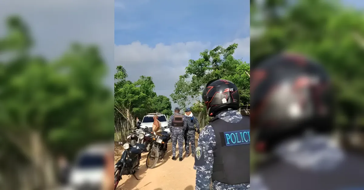 Police officers in tactical gear stand beside parked motorcycles on a dirt road, talking to a shirtless man; a police SUV is in the background.