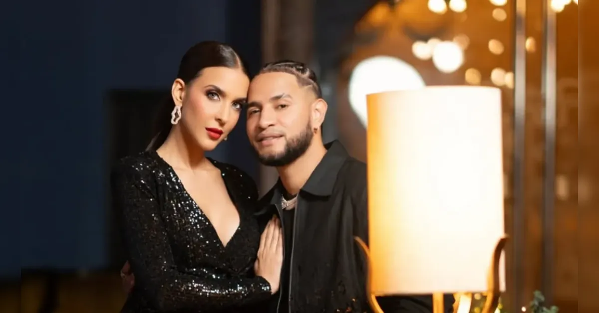 Couple posing together indoors at night; woman in a black sequin dress and man in a dark jacket beside a glowing lamp.