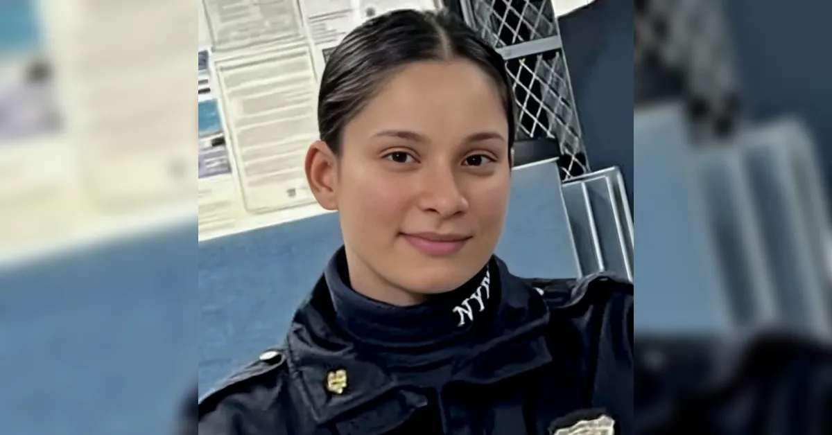 Close-up selfie of a young female police officer in a dark NYPD uniform, with badge and NYPD lettering on the collar, in a station background.