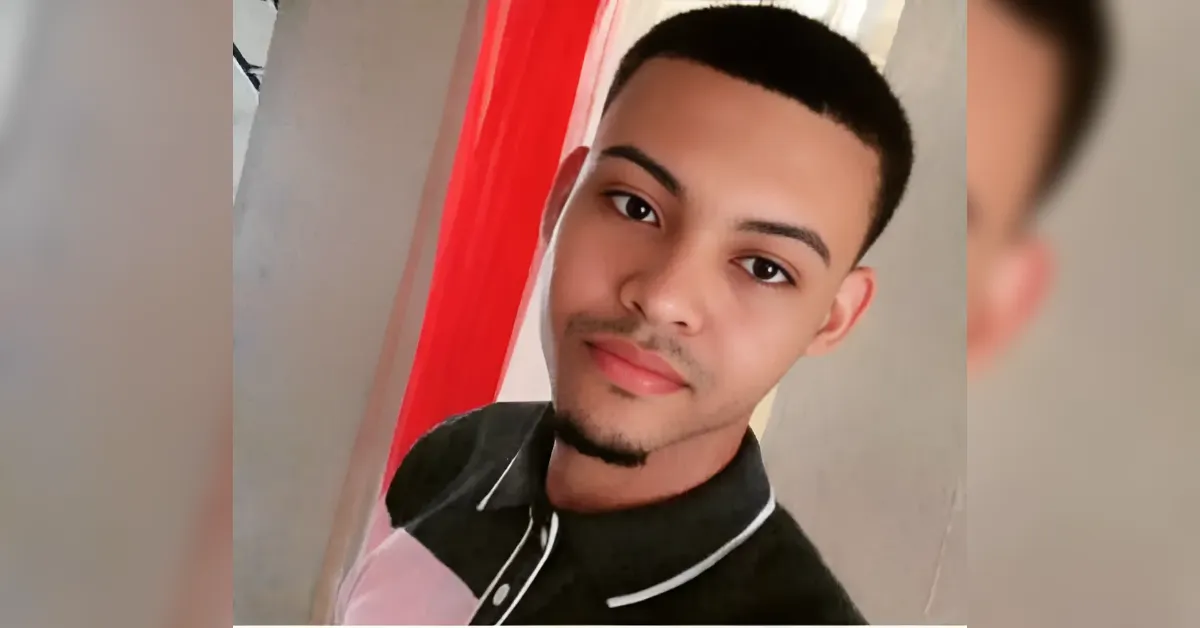 Portrait of a young man taking a selfie indoors, short black hair, light stubble, wearing a black polo with white trim.