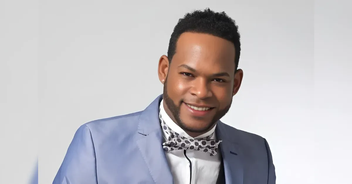 Smiling man in a light blue suit with a patterned bow tie, posing against a gray studio backdrop