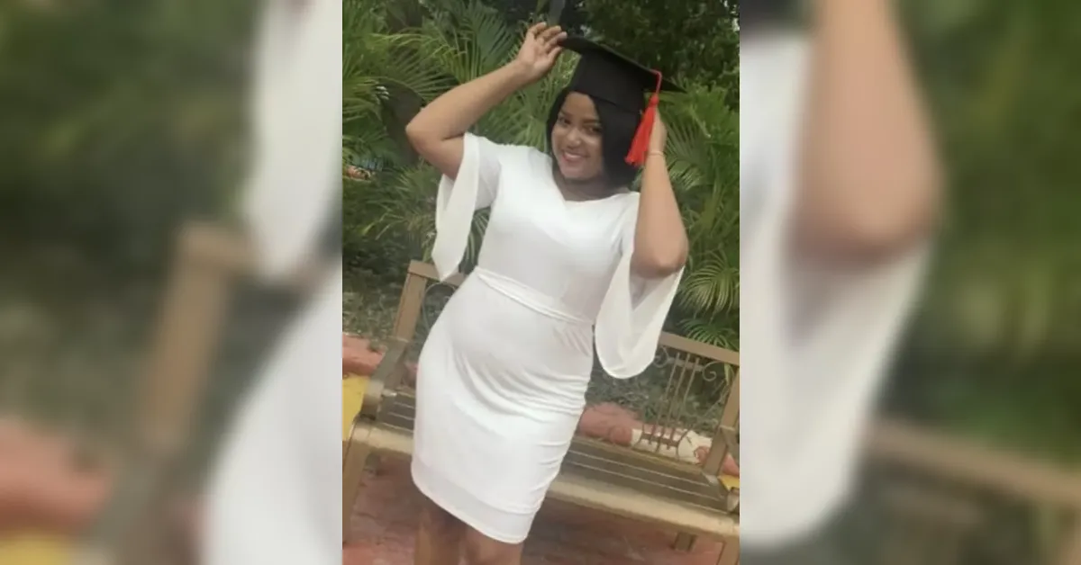Woman in a white dress posing outdoors, adjusting her graduation cap with a red tassel.