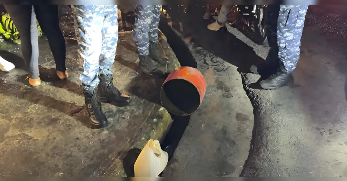 Group of people wearing boots gathers around a broken orange plastic bucket on a wet street surface.