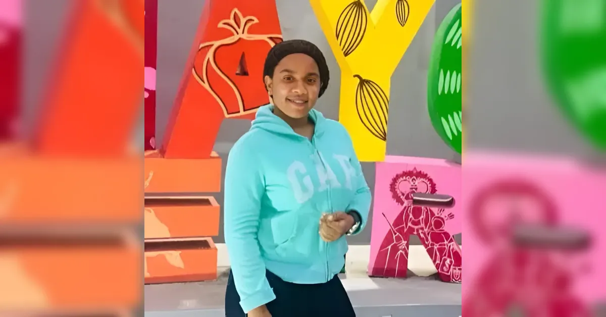 Person in a light blue hoodie poses in front of large, colorful letter sculptures and art shapes in a gallery.
