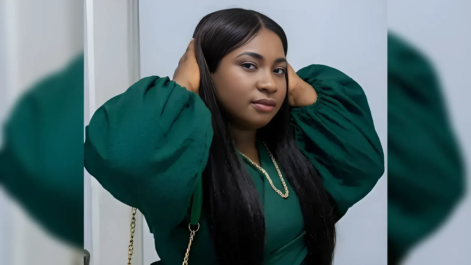 Woman in a dark green blouse with oversized puff sleeves, touching her hair in a posed portrait