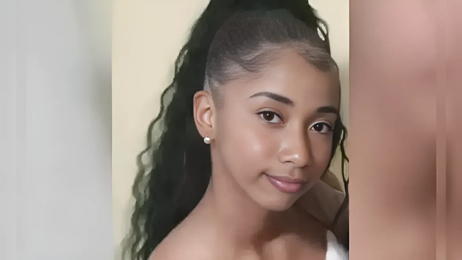 Close-up portrait of a young woman with a high ponytail, pearl stud earrings, and subtle makeup, looking at the camera.