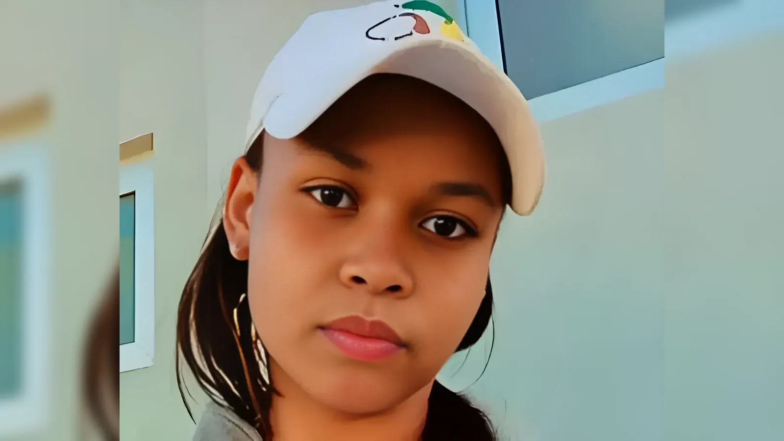 Close-up portrait of a young person wearing a white cap, looking directly at the camera with a neutral expression