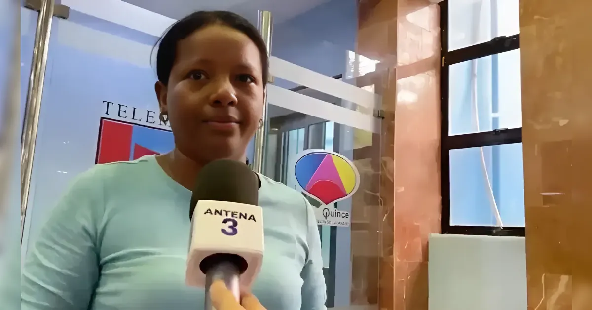 Female reporter holds a microphone labeled 'ANTENA 3' for an interview inside a TV studio with glass walls behind her