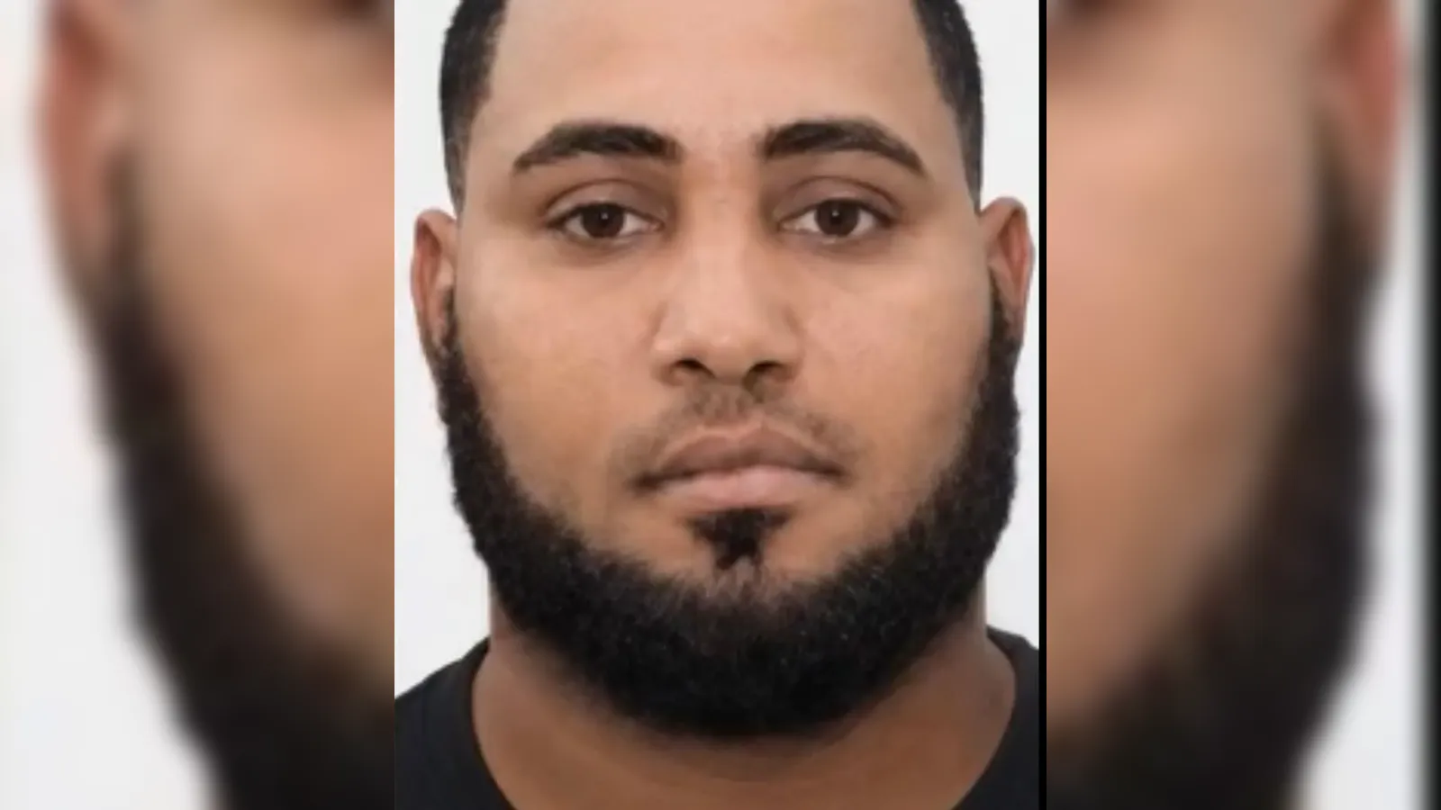 Close-up mugshot of a man with short hair and a full beard facing the camera, neutral expression