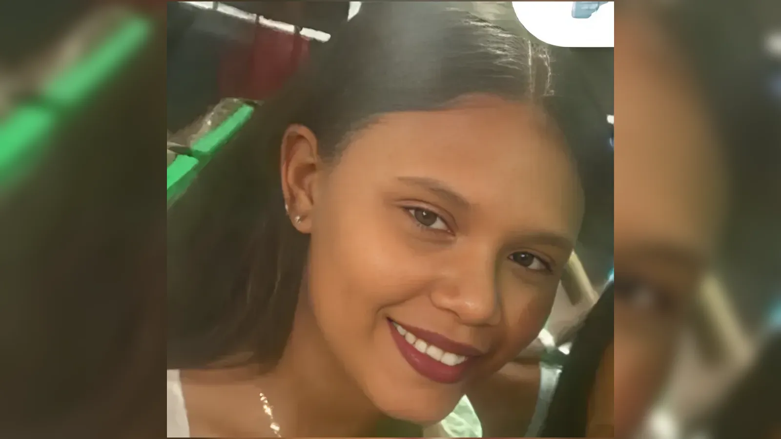 Smiling woman with dark hair, brown lipstick, and small stud earrings in a close-up portrait.