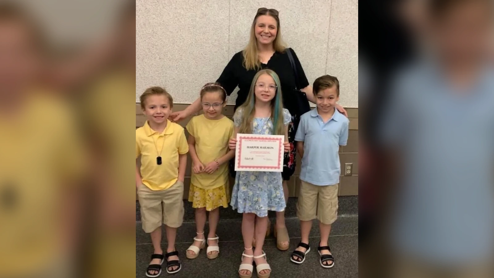 Group of five people posing for a photo indoors; the central girl holds a certificate and smiles regardless.