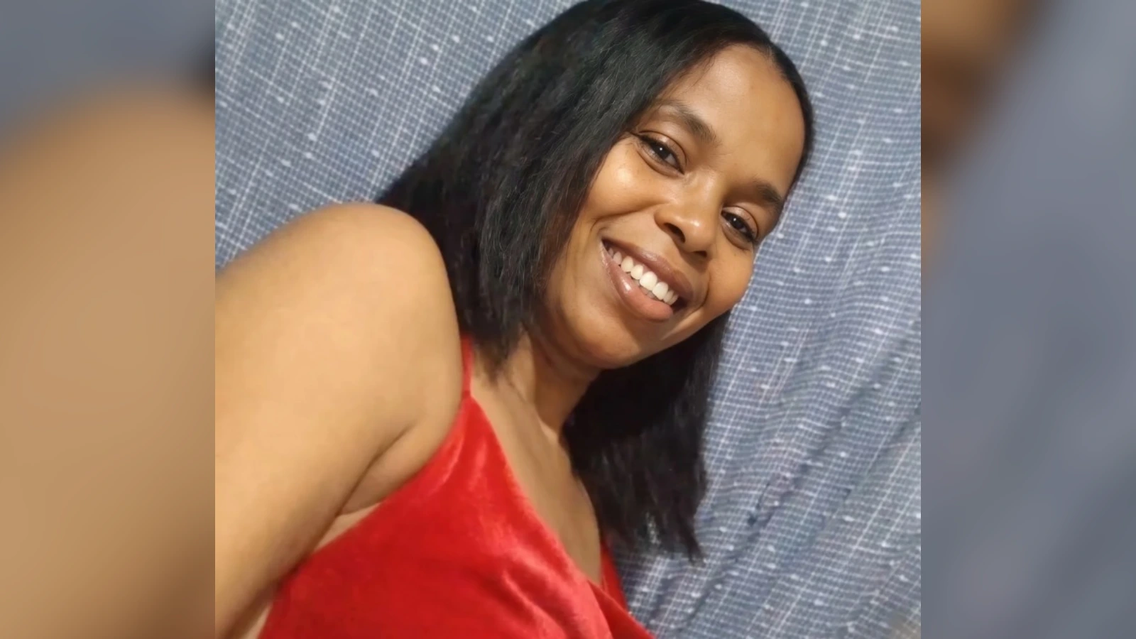 Smiling woman with shoulder-length dark hair wearing a red sleeveless top, in front of a blue patterned backdrop.