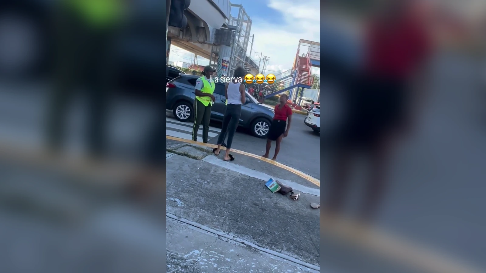 Two women converse with a police officer in a neon-vested uniform on a street, a car parked behind them and scattered items on the curb.”] ,